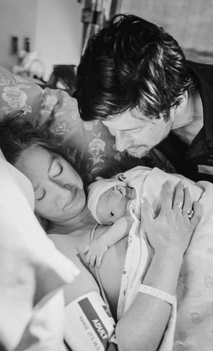 Partner leaning close as new mother holds her sleeping baby