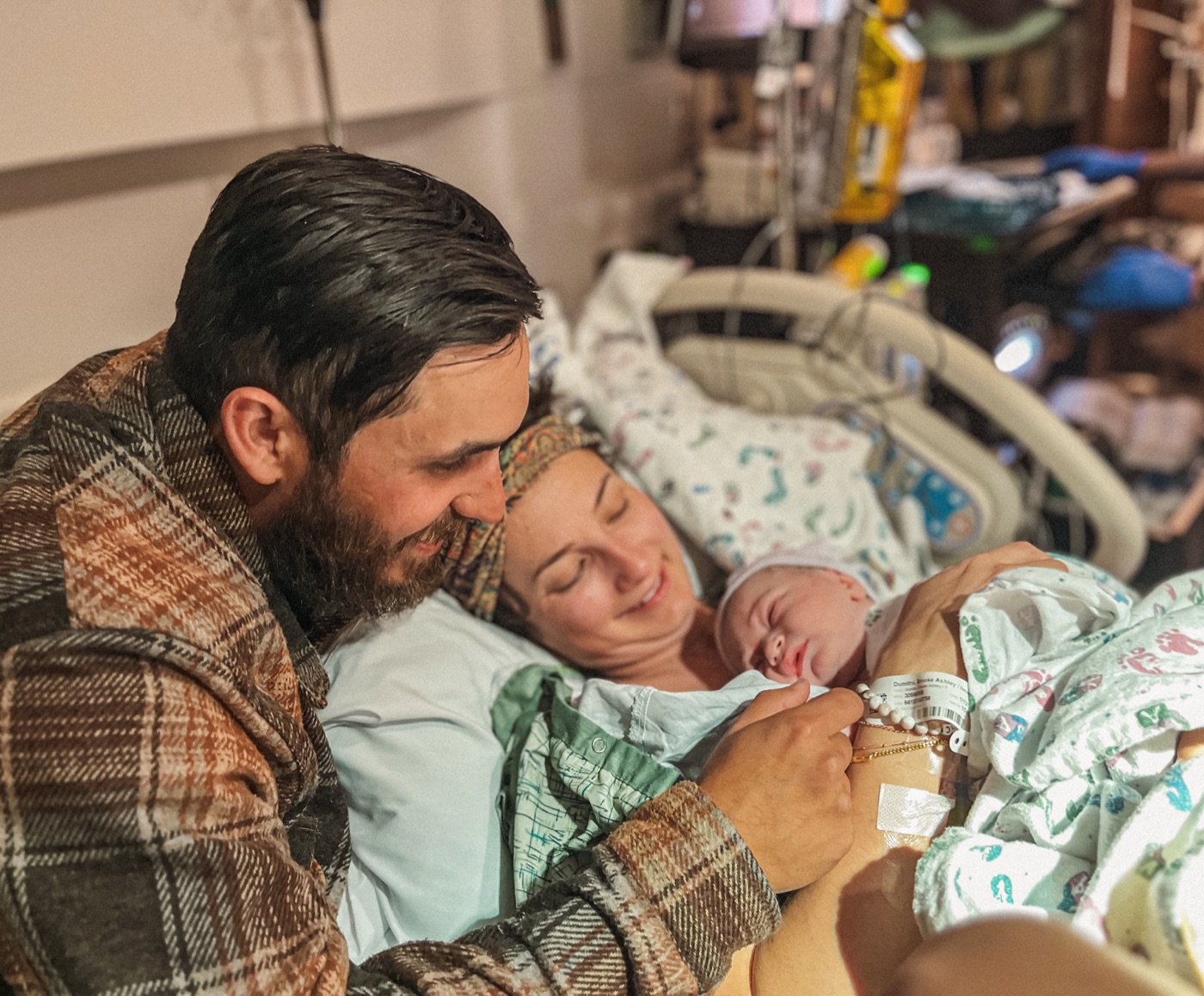 Father and mother resting cheek to cheek with their sleeping newborn