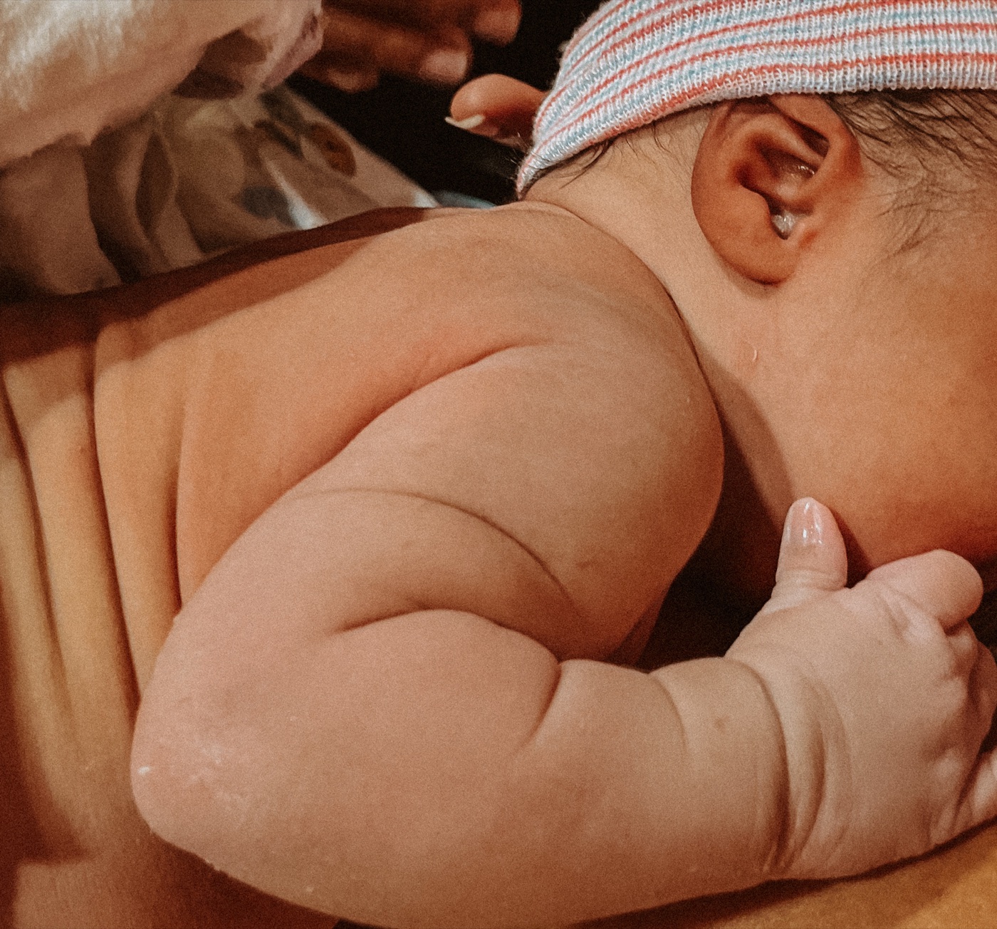 Close-up of a newborn wearing a striped cap snuggled against mother