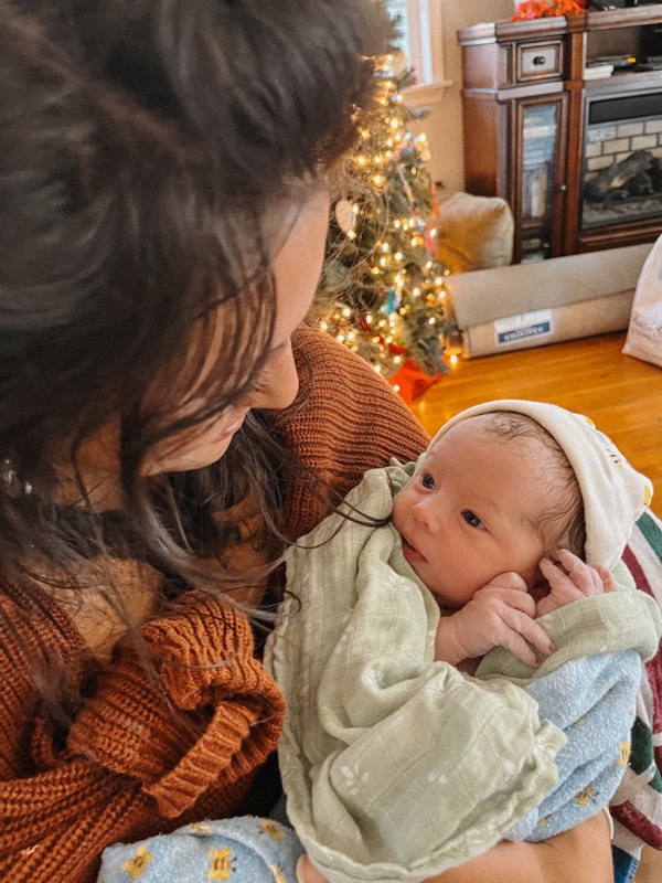 Juliana holding a swaddled newborn by a Christmas tree