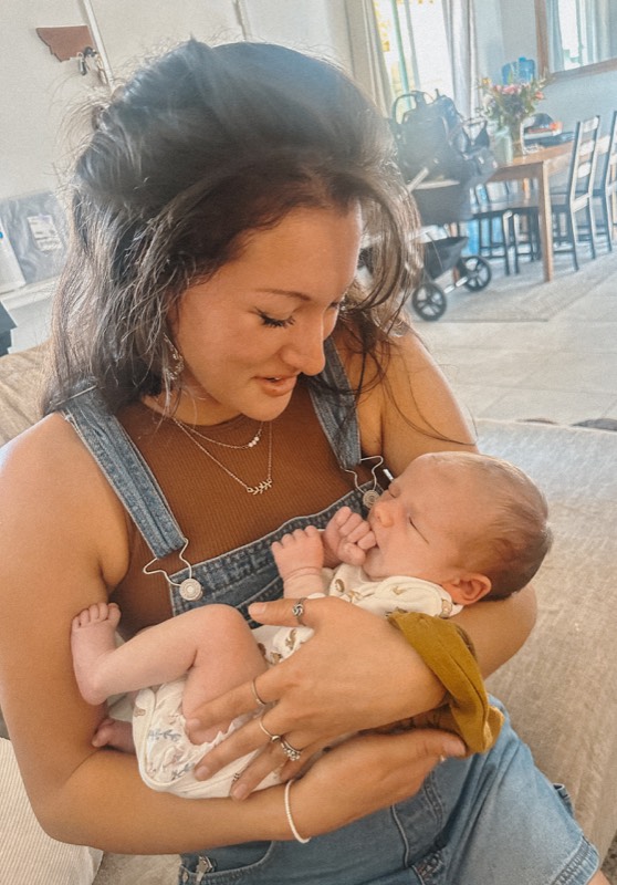 Juliana in overalls smiling down at a sleeping baby